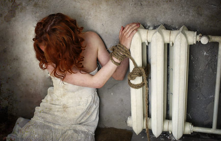 Girl victim of kidnapping sits tied on the floor in an abandoned buildingの写真素材