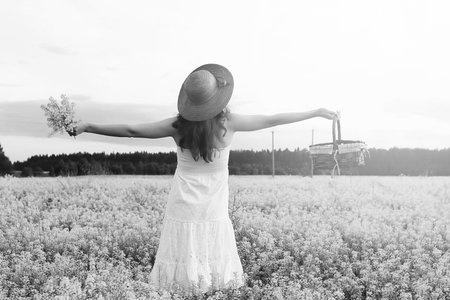 monochrome portrait of young girl in a hat standing in huge field of flowersの写真素材