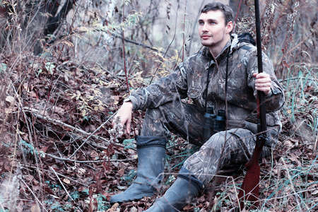 A man in camouflage and with a hunting rifle in a forest on a spの写真素材