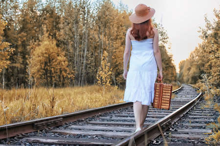 autumn park girl in white sundress and a wicker suitcase walkingの写真素材