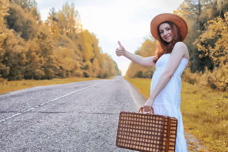 autumn park girl in white sundress and a wicker suitcase walkingの写真素材