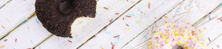 Horizontal bakground of chocolate donuts on a table and a scattering of sweet ornamentsの写真素材