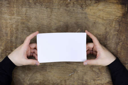 male hands holding a white blank sheet of paper on the background of wooden texture tableの写真素材