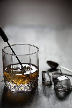 Whiskey in a glass and pieces of ice on a wooden tableの写真素材