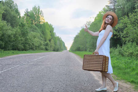 girl in a white sundress and wicker suitcase walking on railsの写真素材