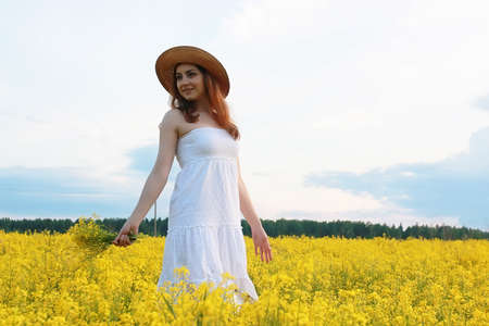 Girl in straw hat in a field of yellow flowers blossomingの写真素材
