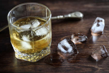 Whiskey in a glass and pieces of ice on a woodの写真素材