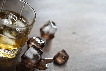 Whiskey in a glass and pieces of ice on a woodの写真素材
