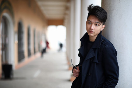 Asian young man in a coat on the streetの写真素材
