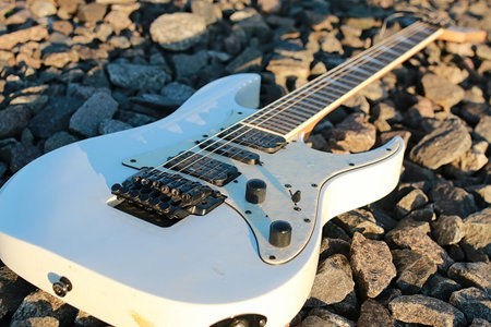white electric guitar on the railroad tracks and stones