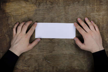 male hands holding a white blank sheet of paper on the background of wooden texture tableの写真素材