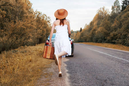autumn park girl in a white sundress and a wicker suitcase walking on railsの写真素材