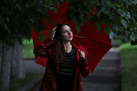 A woman in a red raincoat and umbrella on the street in autumnの写真素材