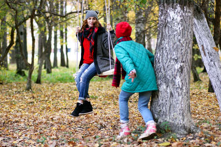 A mom on a swing while the daughter watching in an autumn parkの写真素材