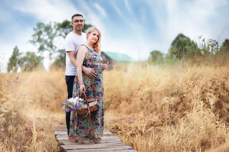 A pregnant girl with big belly and a young man standing on a wooden bridge outdoorの写真素材