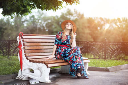A girl in flowery dress sitting on a bench in the parkの写真素材