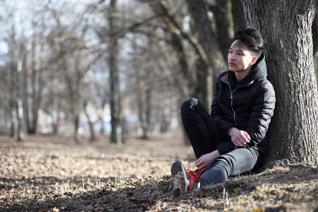 An Asian teenage boy sitting under a tree in natureの写真素材