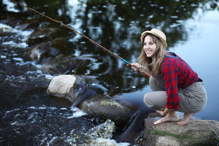 A pretty girl wearing a hat fishing with a rodの写真素材