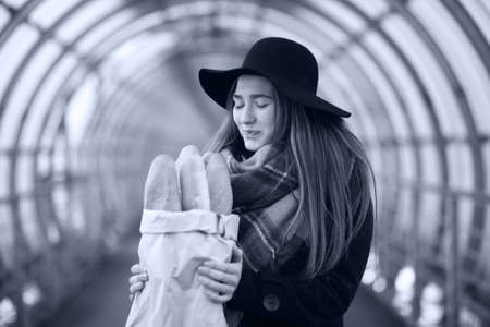 A young lady holding a bag of baguettes in an architectural tunnel in the cityの写真素材