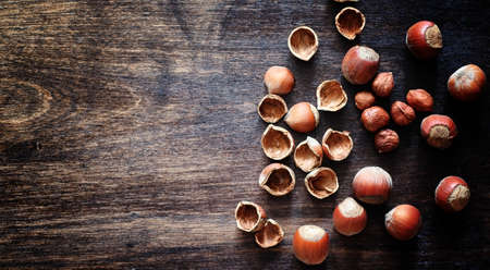 Nuts on a wooden table. Hazelnuts in the shells and shelled. A wooden spoon and nuts on brown table.の写真素材