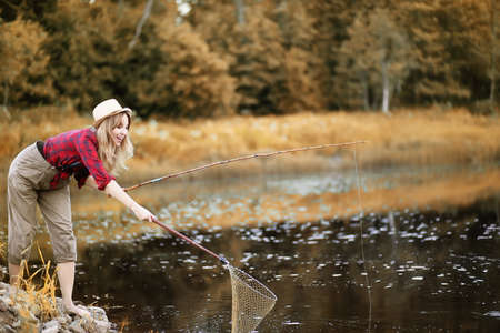 A girl wearing a hat fishing by the river in autumnの写真素材