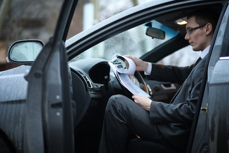 A man in a business suit sitting in the car reading a report