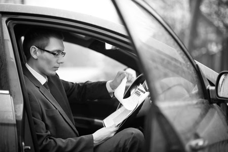 A man in a business suit sitting in the car reading a report