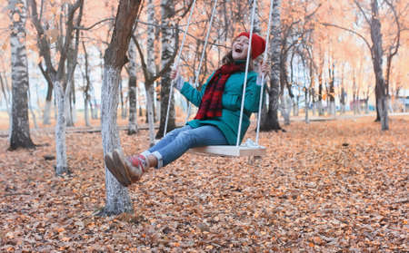 A girl on a swing in autumn city park with leaves on the groundの写真素材