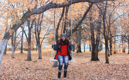 A girl on a swing in autumn city park with leaves on the groundの写真素材