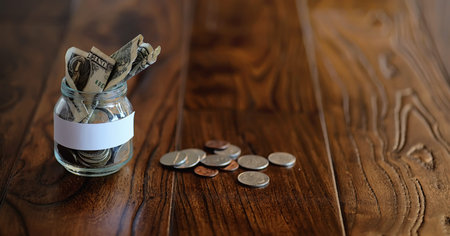 Coins in a glass jar on a wooden floor. Pocket savings from coins in the bank. Piggy bank in a glass jar with coins.の写真素材
