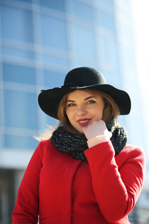 Cute businesswoman in a red coat against a background of glassの写真素材