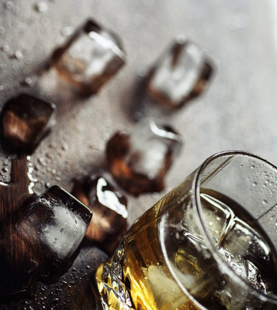 Whiskey with ice with a glass. Cubes of ice on a wooden table and a glass with chilled strong alcohol. Table with American whiskey, bourbon and cards.の写真素材