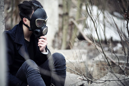 The guy in the coat and gas mask. Post-apocalyptic portrait Asian masked from radiation. The boy is Korean in a mask from poisoning with gases. Post-nuclear mask on the Asian.の写真素材
