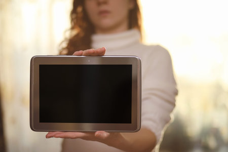 The girl is holding a tablet. The girl has a computer with a screen