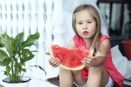 Adorable blonde girl eats a slice of watermelon outdoorの写真素材