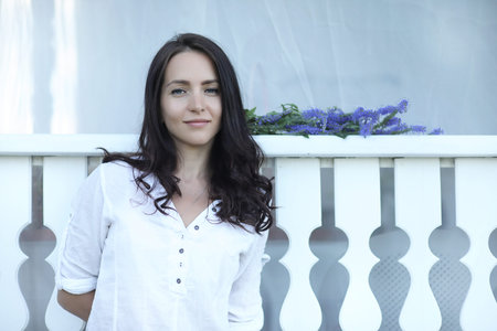 young pretty girl with long brunette hair in vintage black dress in white peas sitting near wooden house in villageの写真素材