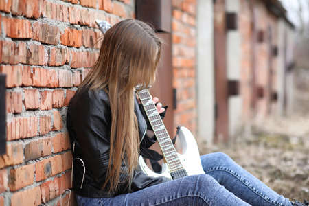 A rock musician girl in a leather jacket with a guitarの写真素材