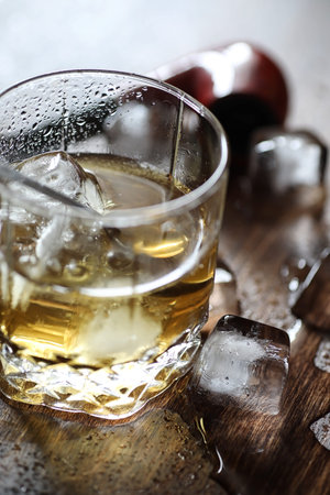 Whiskey in a glass and pieces of ice on a woodの写真素材