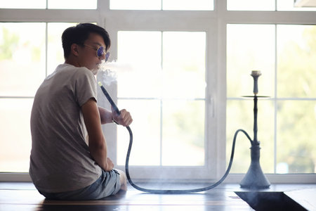 Asian man smoking a hookah at the windowの写真素材