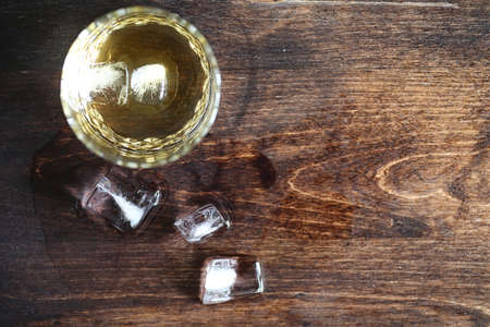 Whiskey in a glass and pieces of ice on a woodの写真素材