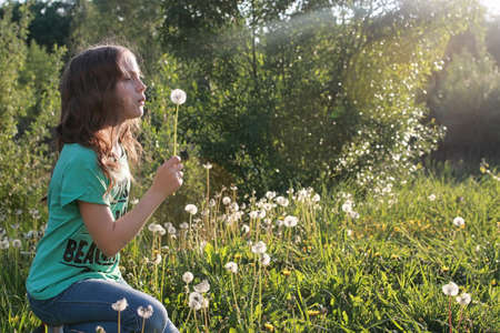 Teen blowing seeds from a dandelion flower in a spring parkの写真素材
