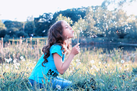 Teen girl blowing seeds from a flower dandelion in spring parkの写真素材