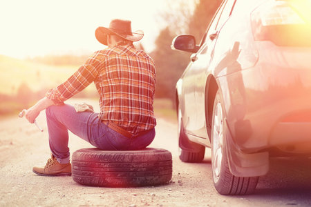 The man is sitting on the road by the car in the nature