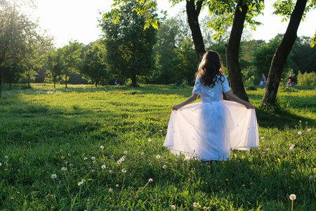 Teen blowing seeds from a dandelion flower in a spring parkの写真素材