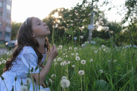 Teen blowing seeds from a dandelion flower in a spring park