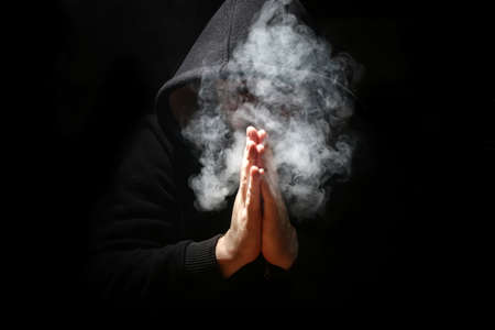 Man in a black hood and smoke on a black backgroundの写真素材