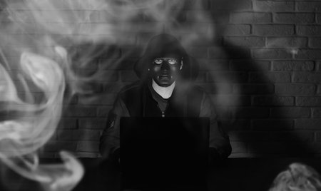Hacker in black mask and hood at the table in front of the monitor