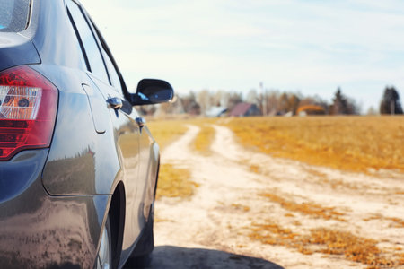The car is parked in the field. The car is driving along the rural road to the house. The car is...