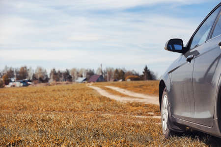 The car is parked in the field. The car is driving along the rural road to the house. The car is gray in the meadow in front of country roadの写真素材