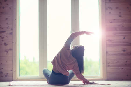 The girl is engaged in yoga on the rug in front of the windowの写真素材